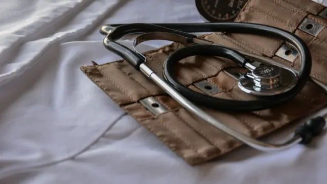 Black stethoscope resting on a brown leather case on a white sheet