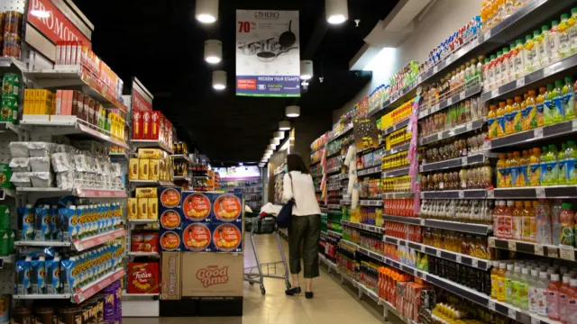 A shopper in a supermarket aisle lined with shelves of drinks and snacks