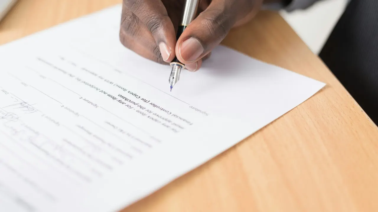 Hand signing a printed document with a pen on a wooden desk