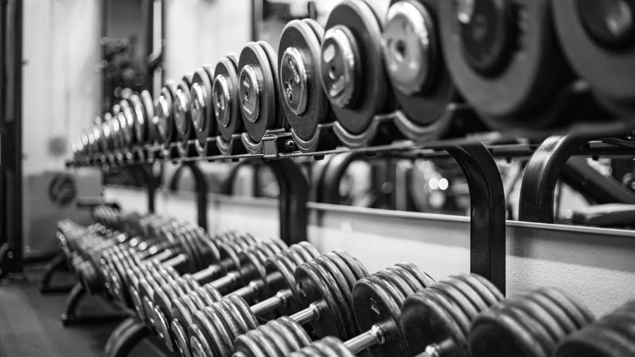 Rows of dumbbells lined up on racks in a gym, in black and white