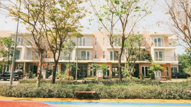 Low-rise modern townhouses behind a row of young trees and a landscaped garden