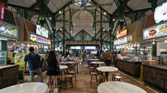 Diners walking between rows of food stalls and tables in a busy food centre