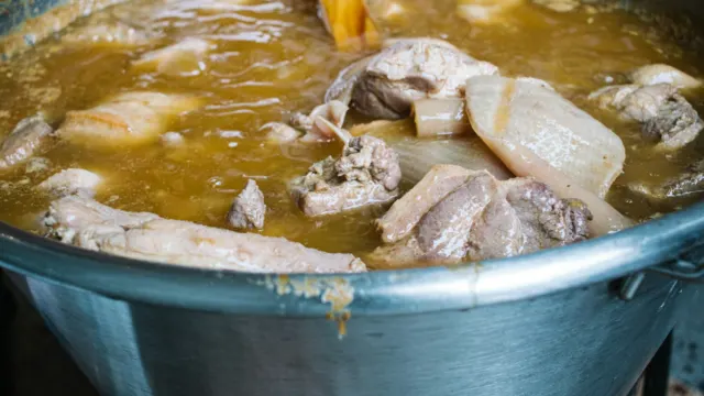Pork bones and meat simmering in a large steel pot of broth