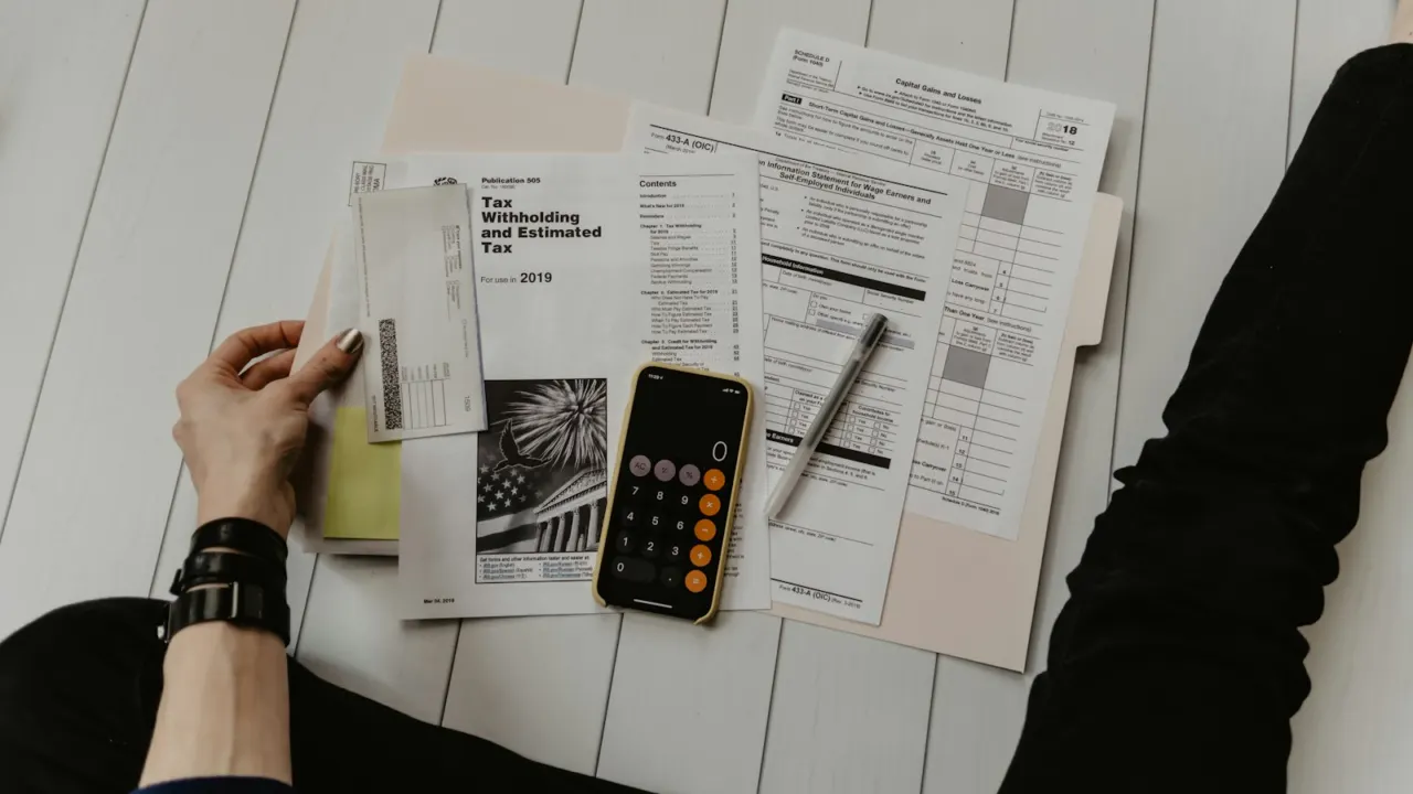 Person holding a printed statement beside a pen and calculator on a desk