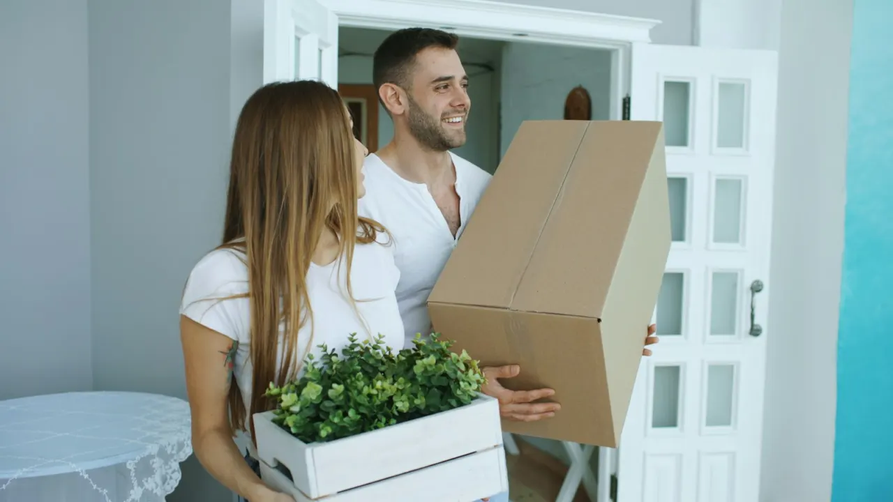 Couple carrying cardboard moving boxes into a new home