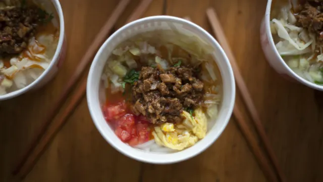 Three bowls of noodle soup with minced meat and chopsticks on a wooden table