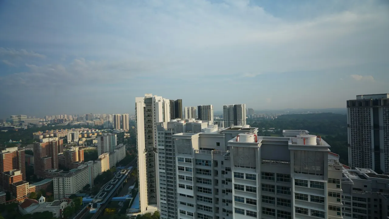 High-rise HDB estates and green trees seen from a high floor under a pale sky