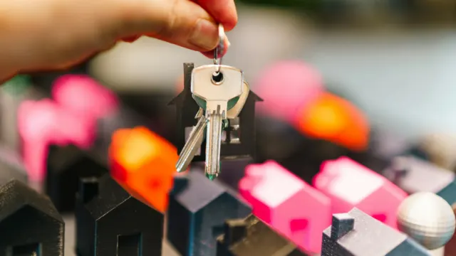 Hand holding a set of house keys above small model houses
