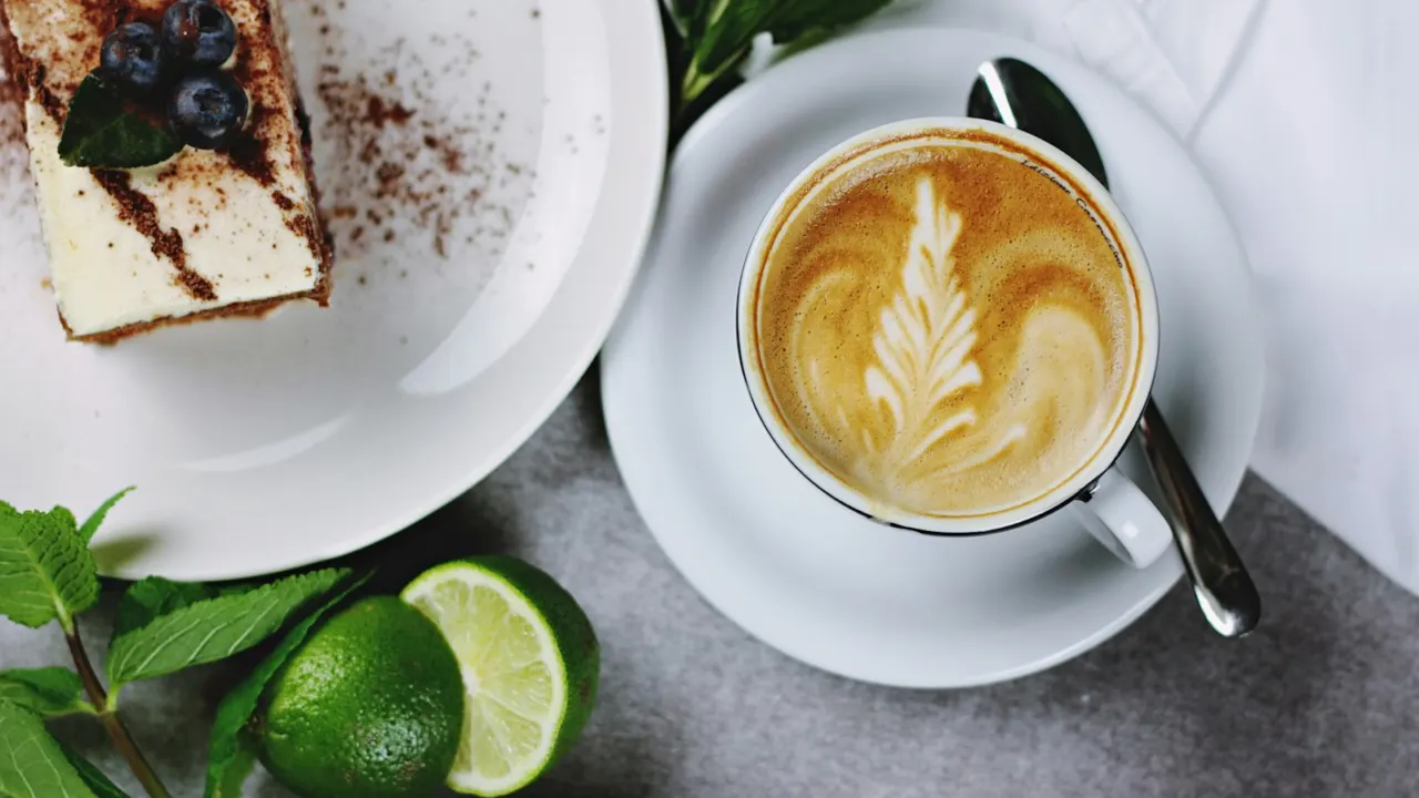 Flat lay of a latte with leaf art beside a slice of layered cake and fresh mint