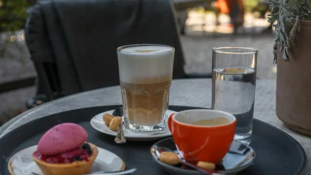 A latte, an espresso and a pink macaron-style dessert on a round outdoor café table