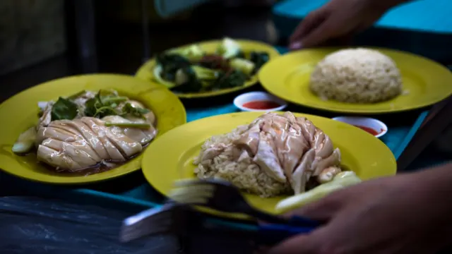 Plates of Hainanese steamed chicken and rice at a hawker table