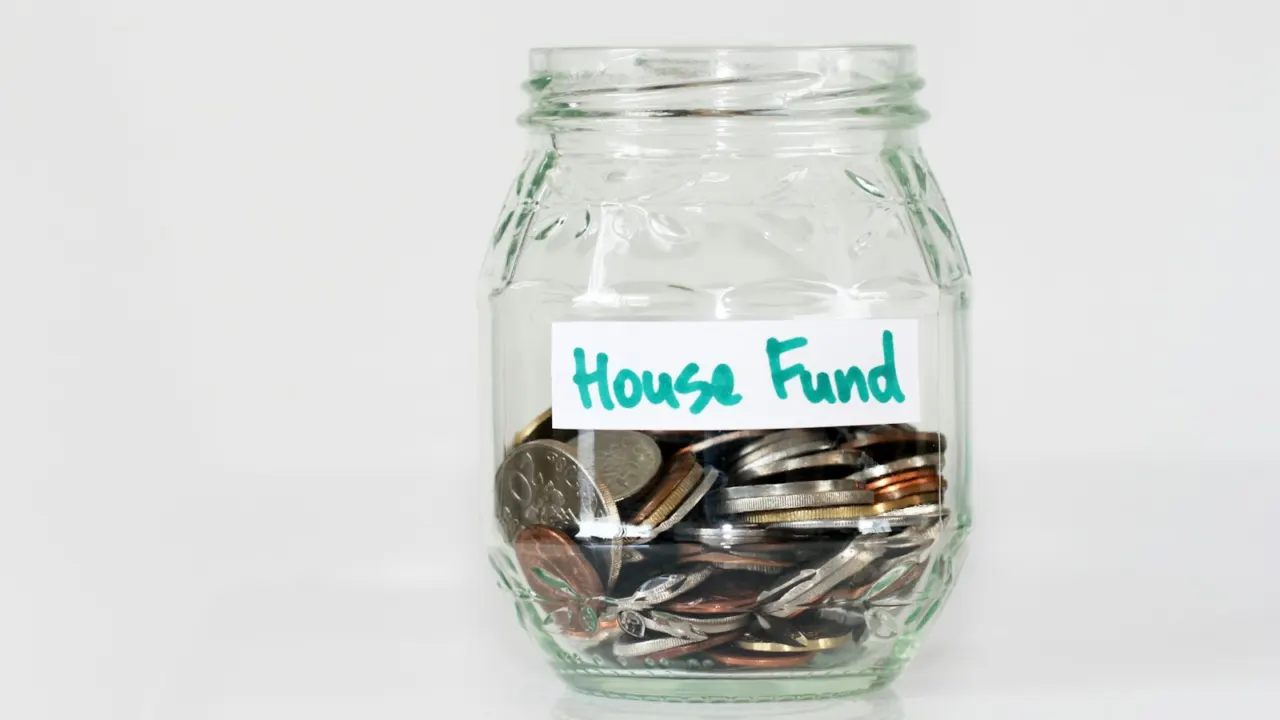 Coins in a clear glass jar labelled house fund