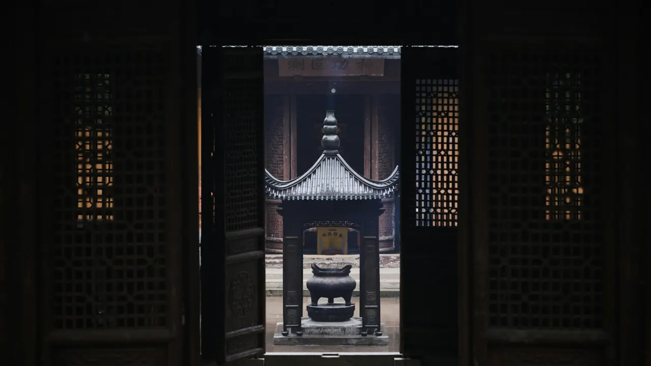 Carved dark wooden doors open onto a sunlit courtyard with a traditional incense burner