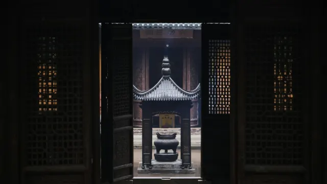 Carved dark wooden doors open onto a sunlit courtyard with a traditional incense burner