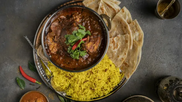 Pot of curry beside yellow rice and folded flatbread on a dark table