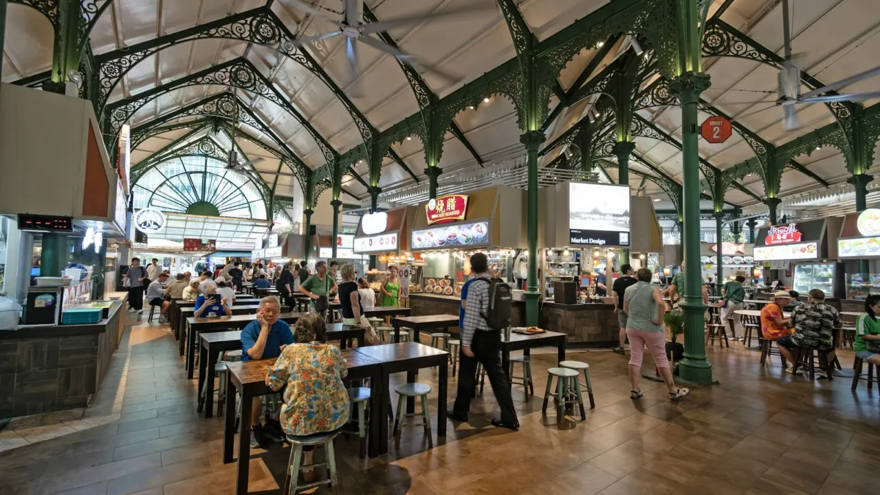 Rows of tables and chairs under a high vaulted roof in a Singapore hawker centre