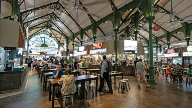 Rows of tables and chairs under a high vaulted roof in a Singapore hawker centre