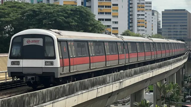 Red and white MRT train on an elevated track beside trees and housing blocks in Singapore