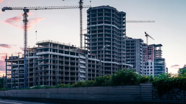 High-rise residential blocks under construction with tower cranes against a pink evening sky