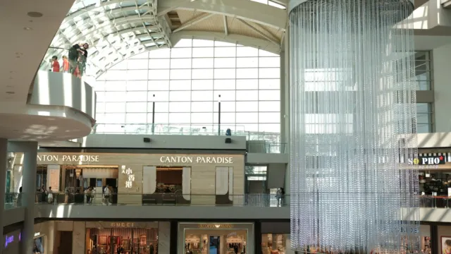 Glass-roofed shopping mall atrium with shopfronts on several levels and a tall water feature