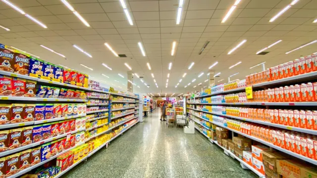 Long, brightly lit supermarket aisle lined with shelves of cereal and groceries