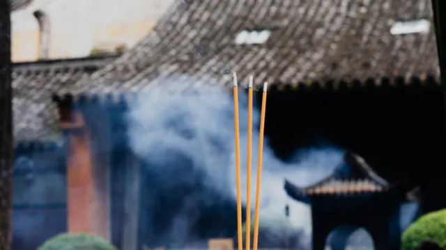 Incense sticks burning with smoke drifting in front of a traditional Chinese temple roof