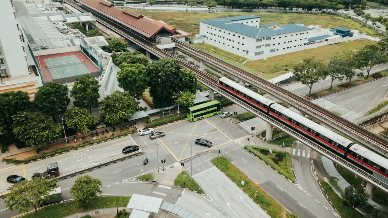 Aerial view of an elevated train line running between low buildings, roads and green fields