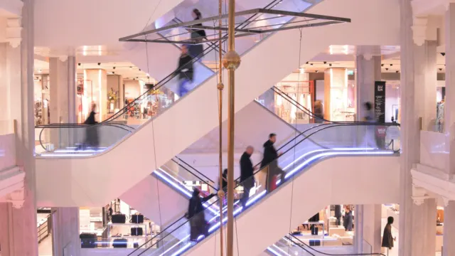 Criss-crossing escalators in a bright multi-level mall atrium, with shoppers riding between floors