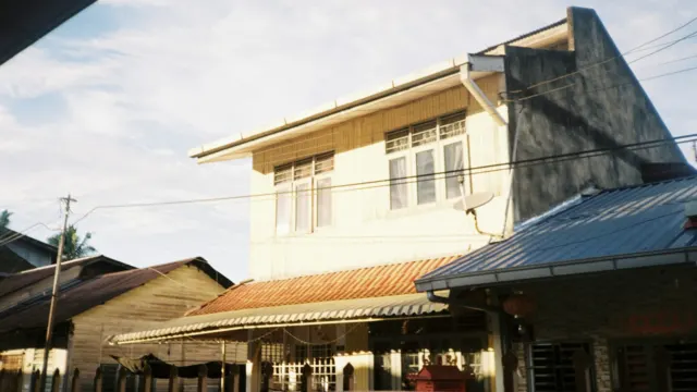 Old two-storey house with corrugated metal roofs and overhead wires under a bright sky