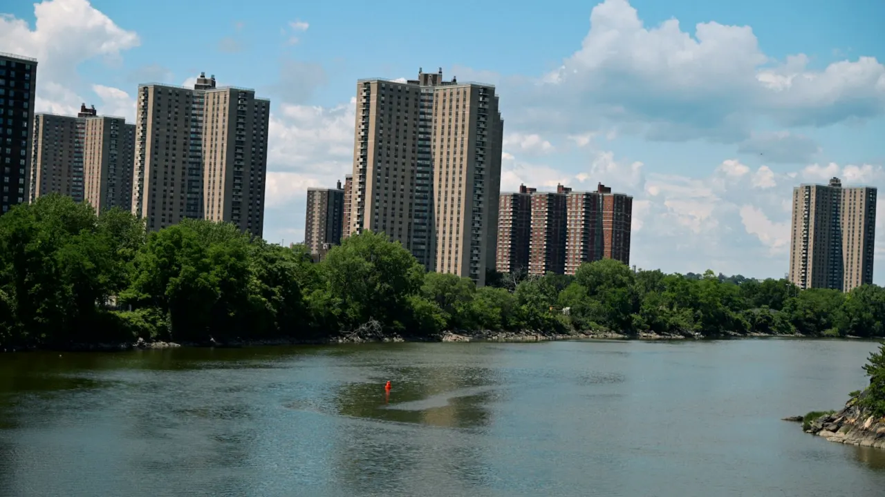 Apartment towers along a tree-lined river under a blue sky