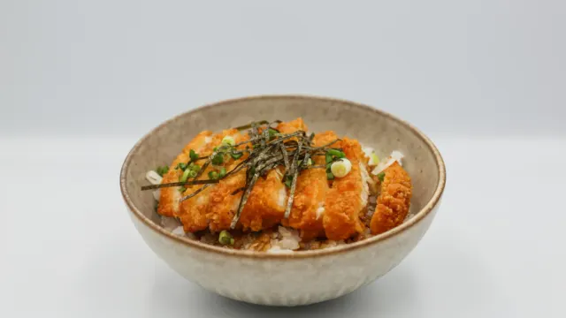 Bowl of rice topped with glazed chicken, seaweed and sesame