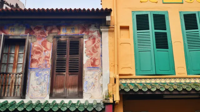 Colourful low-rise shophouse facades with wooden shutters and a tiled awning