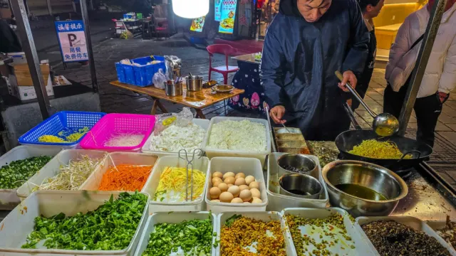 Cook tossing noodles in a flaming wok at a night market food stall