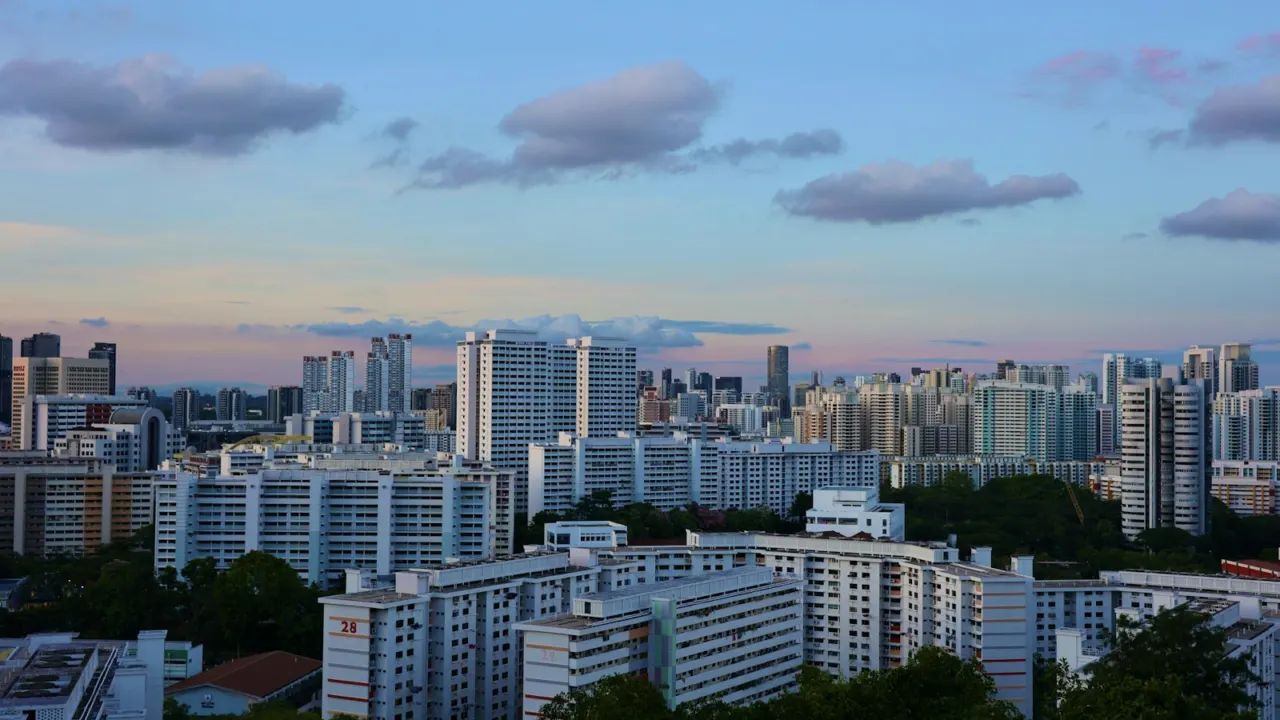 Rows of Singapore HDB blocks and green trees under a blue evening sky