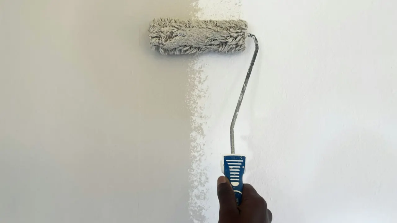 Paint roller applying white paint to a bare interior wall