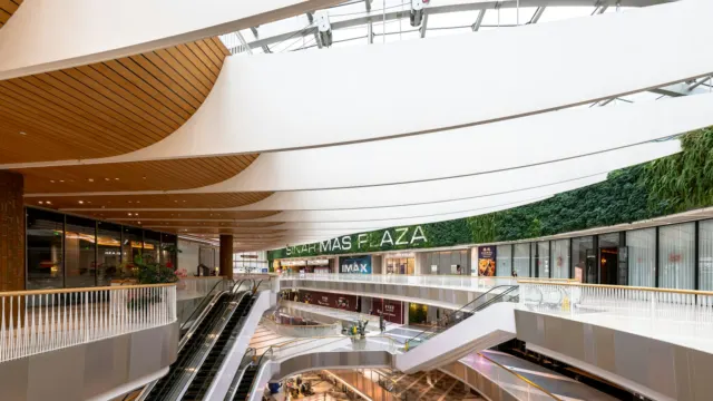 Multi-level shopping mall interior with escalators, glass balustrades and a green wall