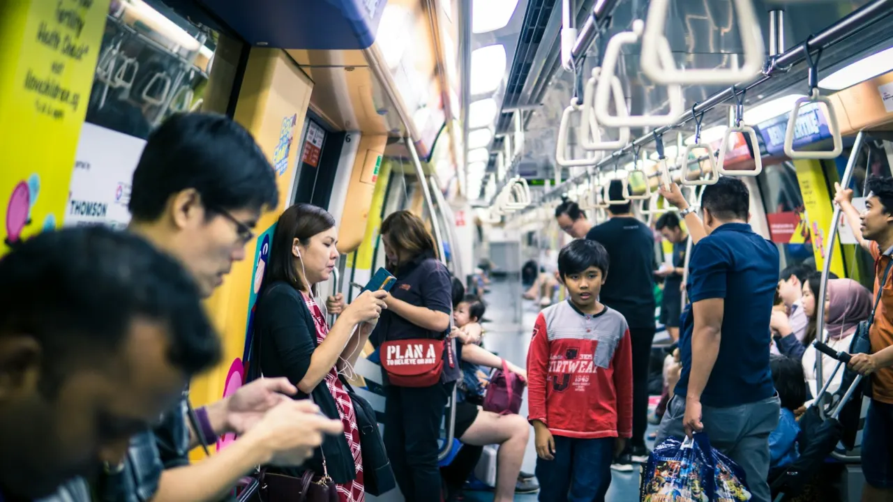 Commuters standing and sitting in a busy MRT train carriage in Singapore