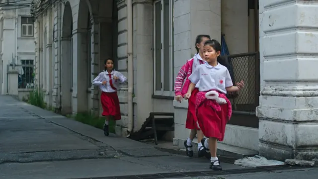 Two young schoolgirls in red and white uniforms walking along a covered walkway