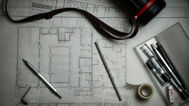 Architectural floor plan drawings on a desk with drafting pencils and a ruler