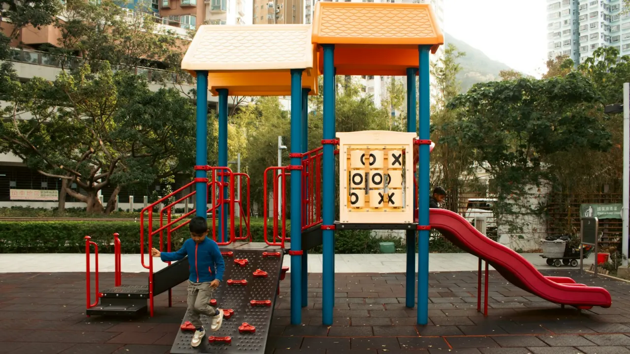 Child climbing a colourful playground structure with a noughts-and-crosses panel in a housing estate