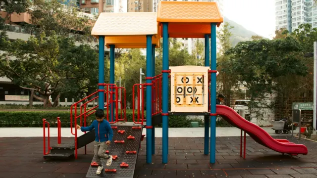 Child climbing a colourful playground structure with a noughts-and-crosses panel in a housing estate