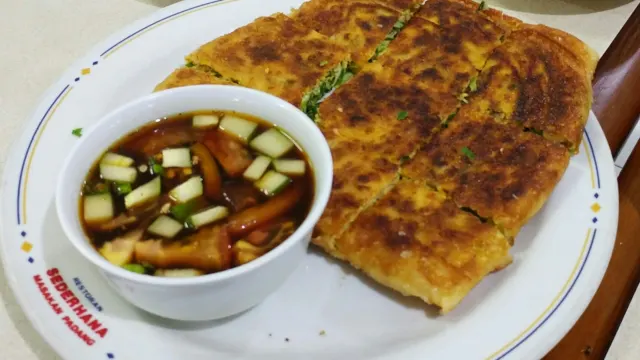 Golden murtabak cut into squares, served with a small bowl of pickled onion and cucumber