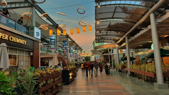 Open-air shopping street with planters, overhead canopies and people walking between shops