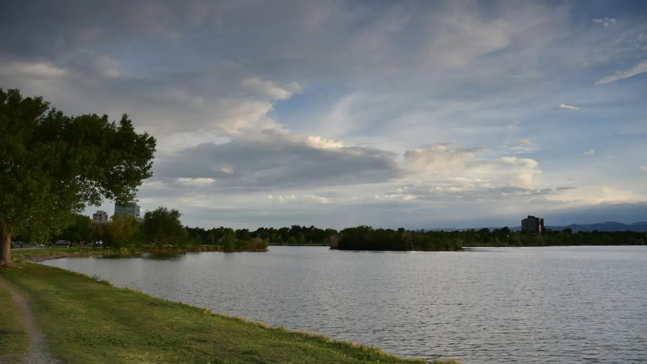 Calm lake with grassy banks and trees under a cloudy sky