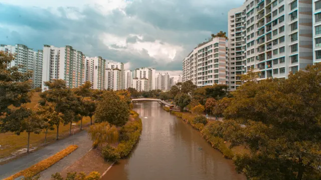 Tree-lined canal with a riverside path running between high-rise HDB blocks
