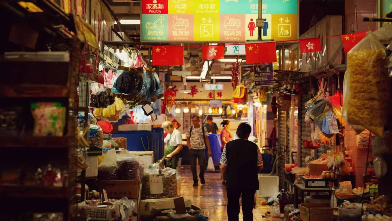Busy indoor market lane lined with stalls selling household goods and produce