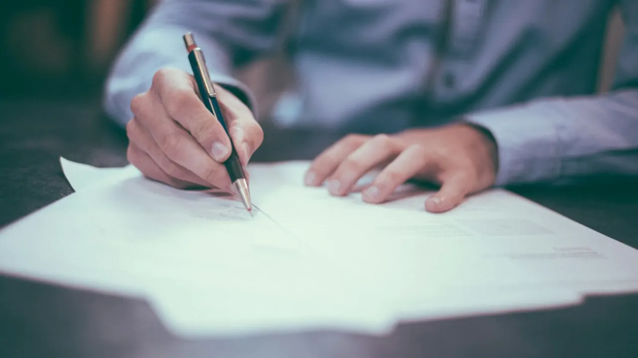 Man signing paperwork at a desk with a pen