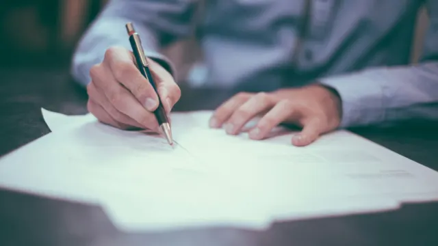 Man signing paperwork at a desk with a pen