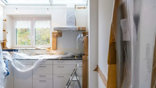 Kitchen under renovation with new white cabinets wrapped in protective plastic