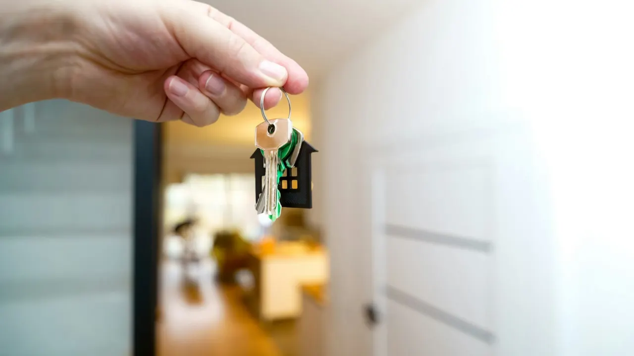 Hand holding a set of house keys at the entrance of a bright apartment